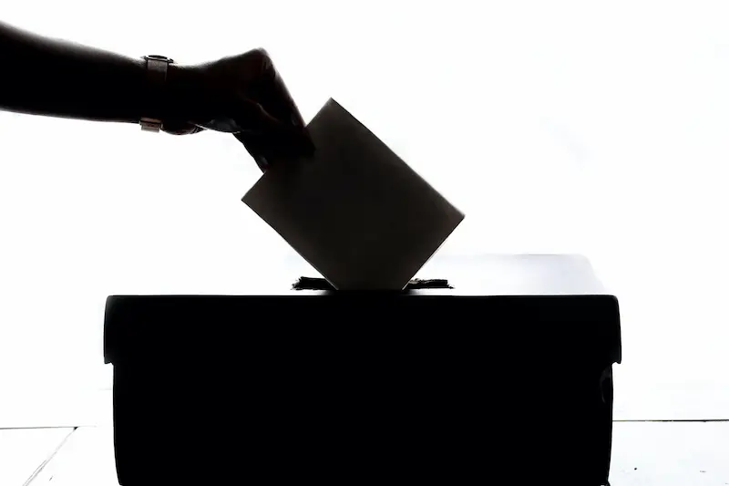 Hand placing a ballot into a voting box